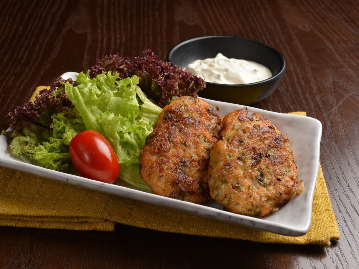 Mshat Zahrah knuspige Blumenkohl-Taler aus Palästina auf weißem Teller mit Salat auf Holzbrett. Oben eine Schale mit Dip. Frontalansicht.