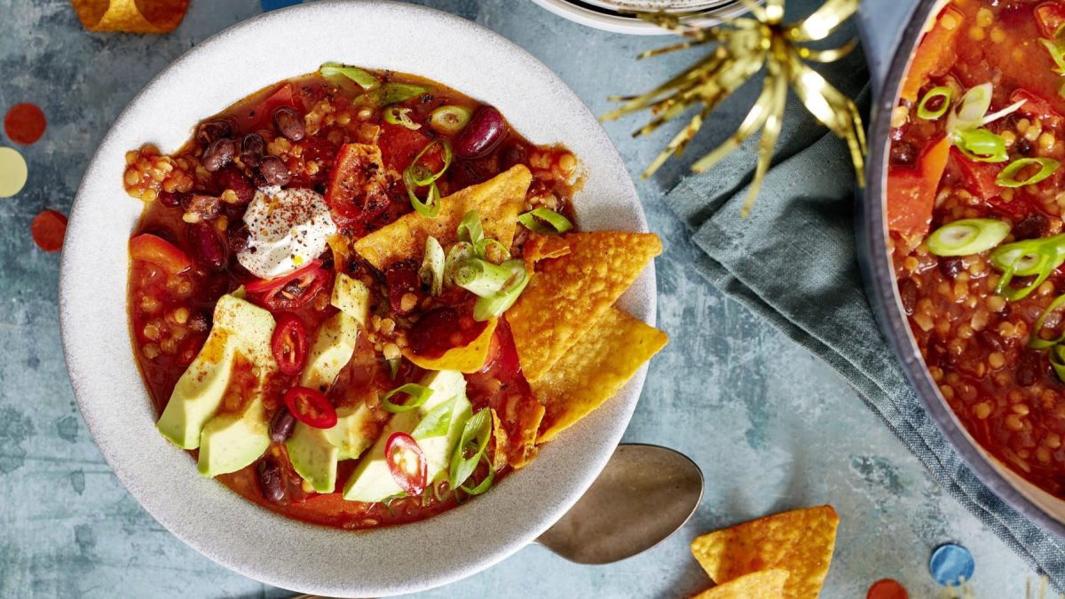 Ein Teller Nacho-Bohnen-Topf mit Schmand, Avocado und Tortillachips in der Draufsicht.