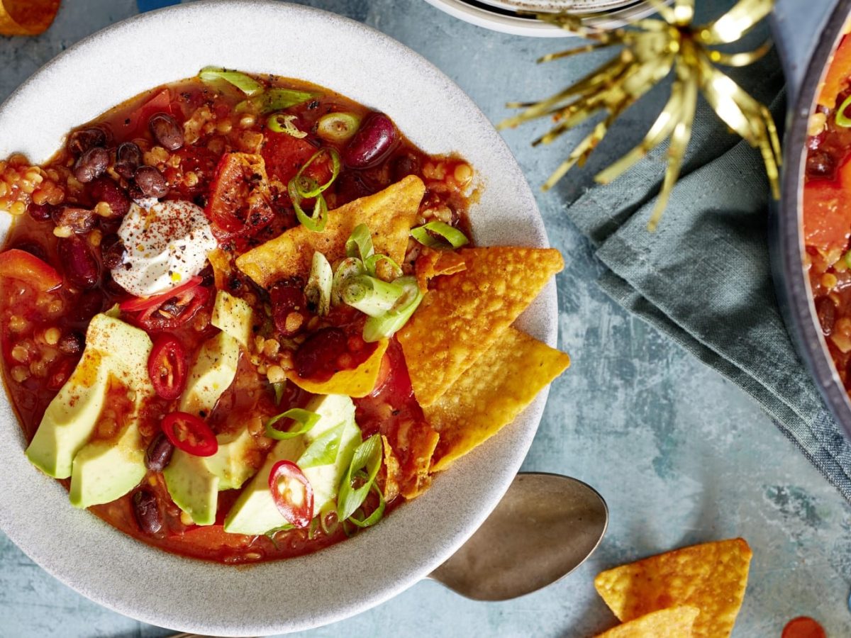 Ein Teller Nacho-Bohnen-Topf mit Schmand, Avocado und Tortillachips in der Draufsicht.