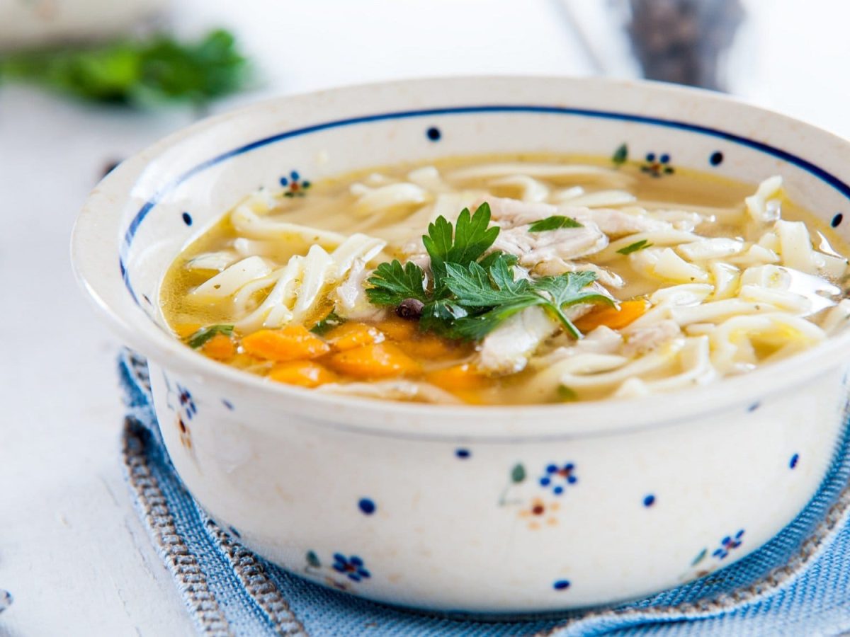 Eine gemusterte Schüssel Nudelsuppe mit Gemüse und Petersilie.