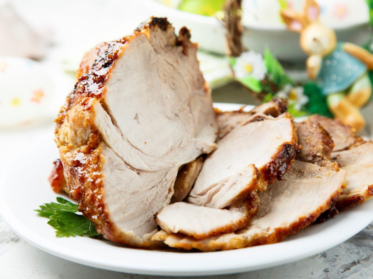 Osterbraten mit Honigglasur auf weißem Teller und hellem Untergrund. Im Hintergrund Deko. Frontalansicht.