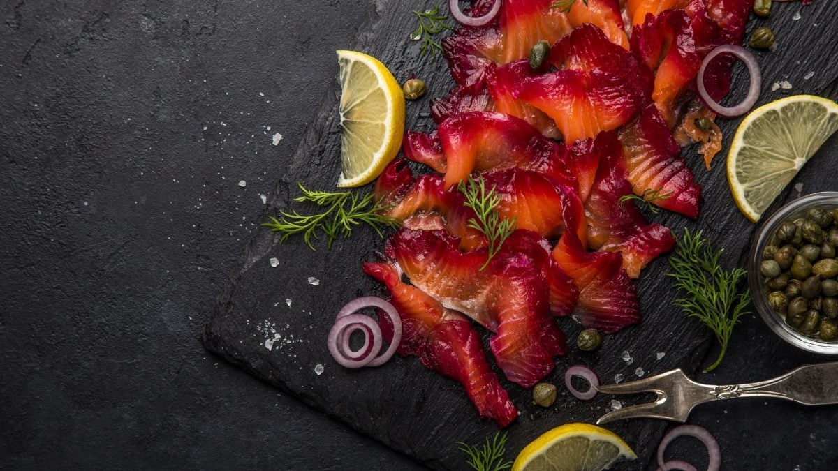 Der in Rote-Bete gebeizte Lachs aufgeschnitten auf einer schwarzen Schieferplatte mit Kapern und Zitronenscheiben.