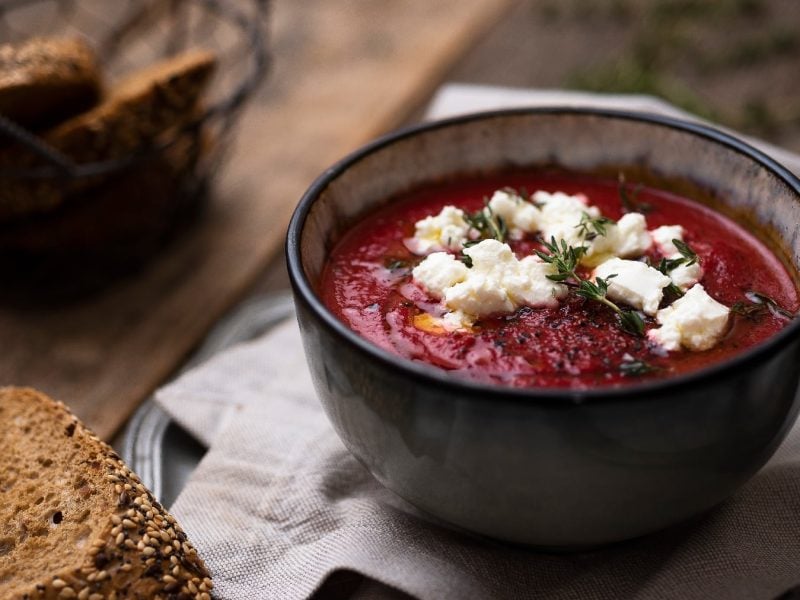 Eine schwarze Schale mit der Rote Bete Suppe und Ziegenkäse auf einem dunklen Holztisch mit ein paar Scheiben dunklem Brot.