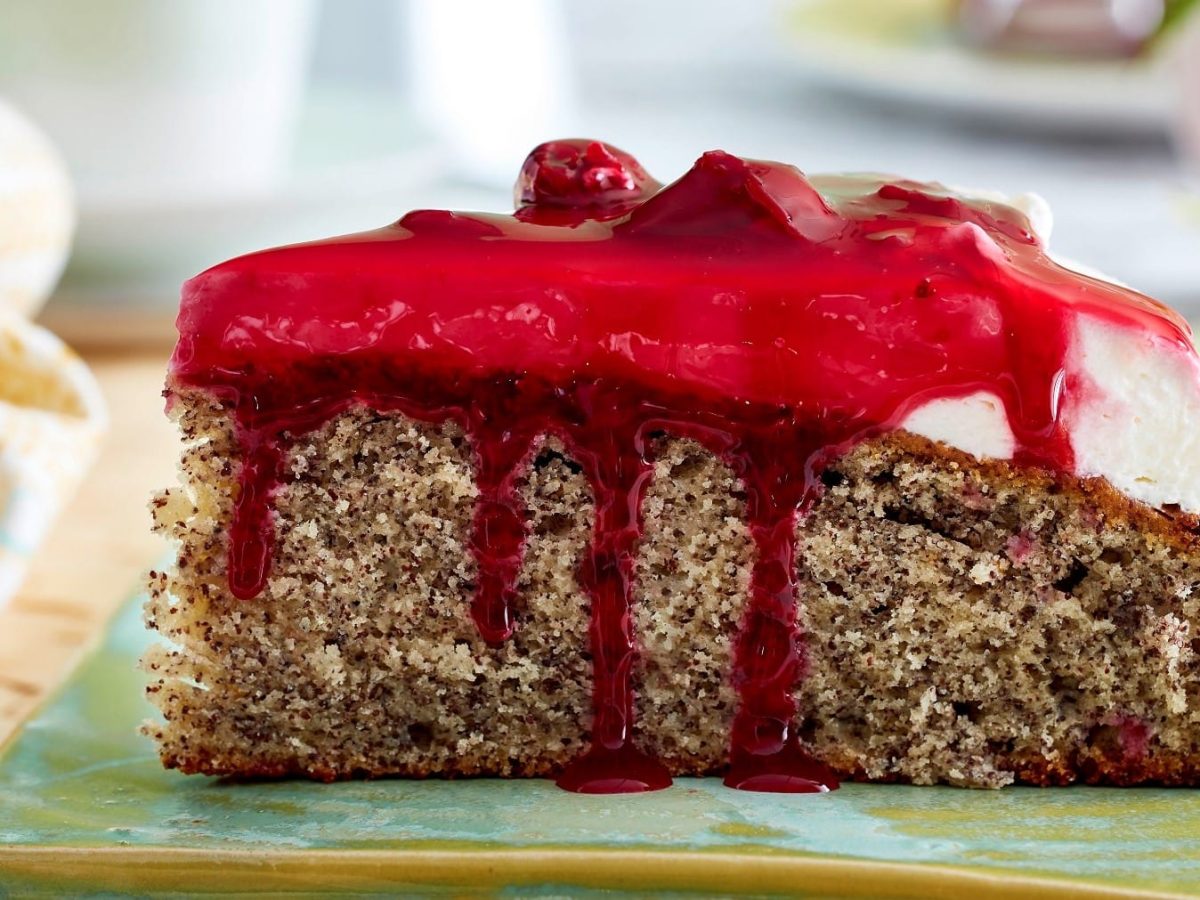 Ein Stück Rote-Grütze-Mohnkuchen von der Seite auf grünem Untergrund.