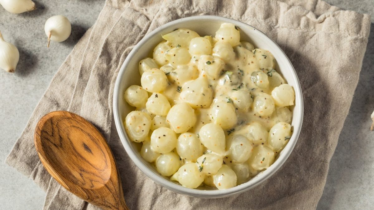 Eine kleine Schüssel mit Creme-Perlzwiebeln auf einem grauen Tuch.