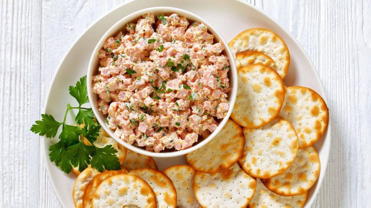 Schinkensalat in weißer Schale mit Crackern.