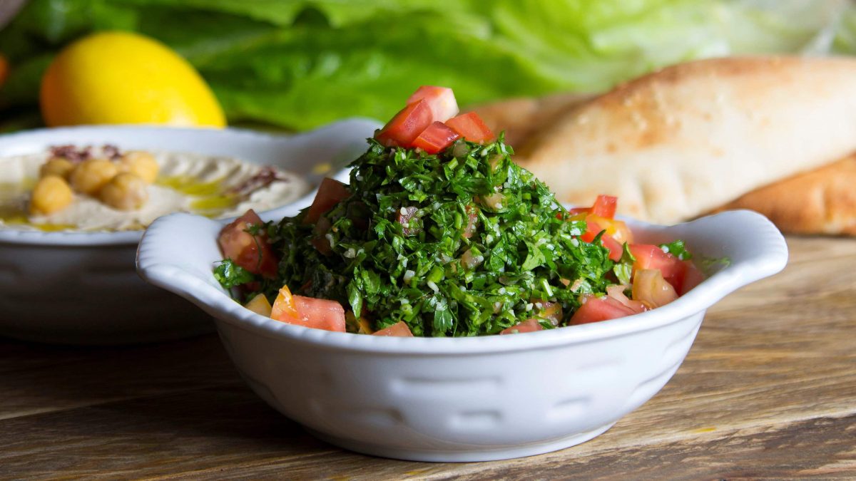 Persischer Shirazi Salat in weißer Salatschale auf Tisch mit diversen Speisen. Frontalansicht.