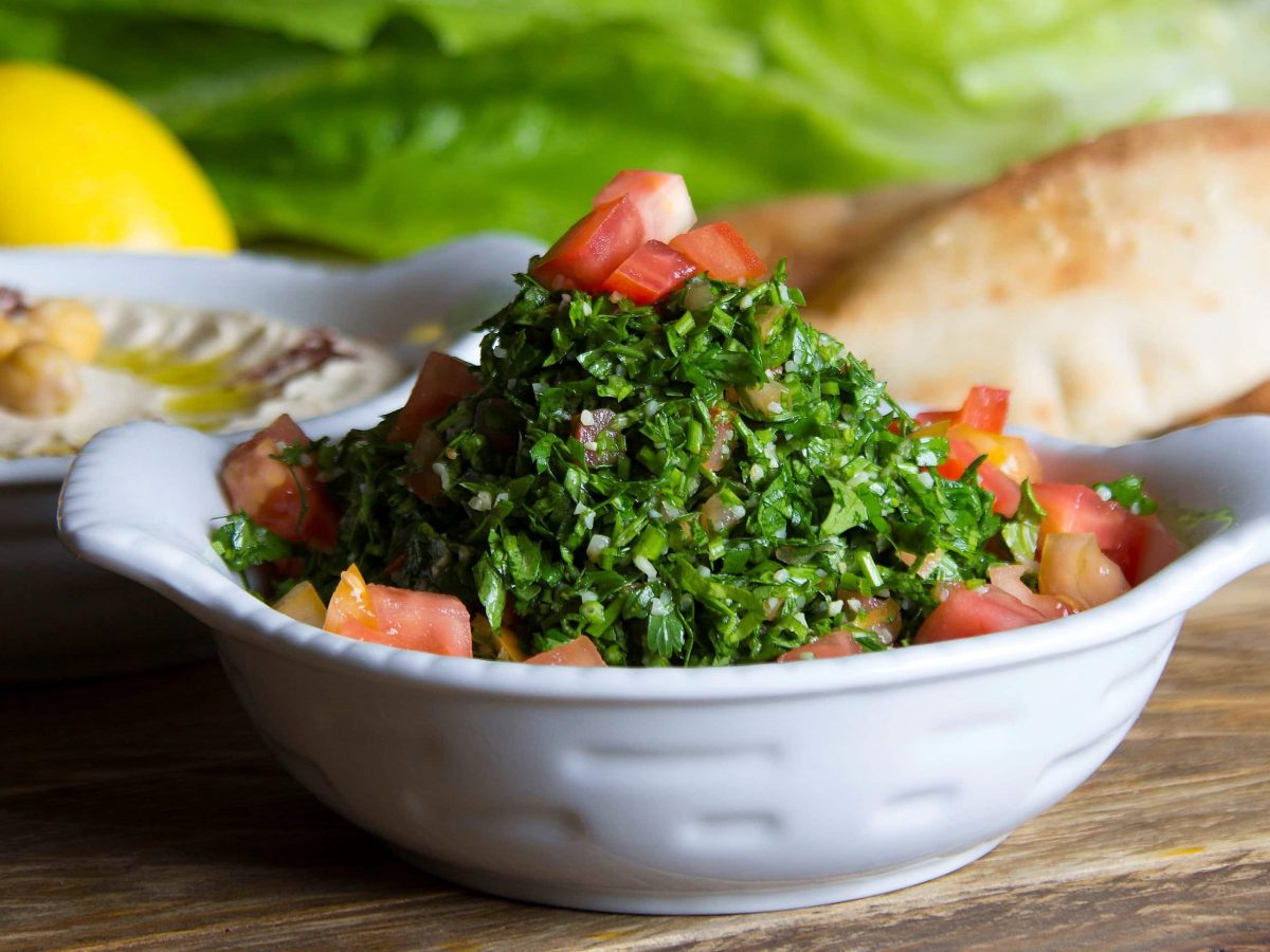 Persischer Shirazi Salat in weißer Salatschale auf Tisch mit diversen Speisen. Frontalansicht.