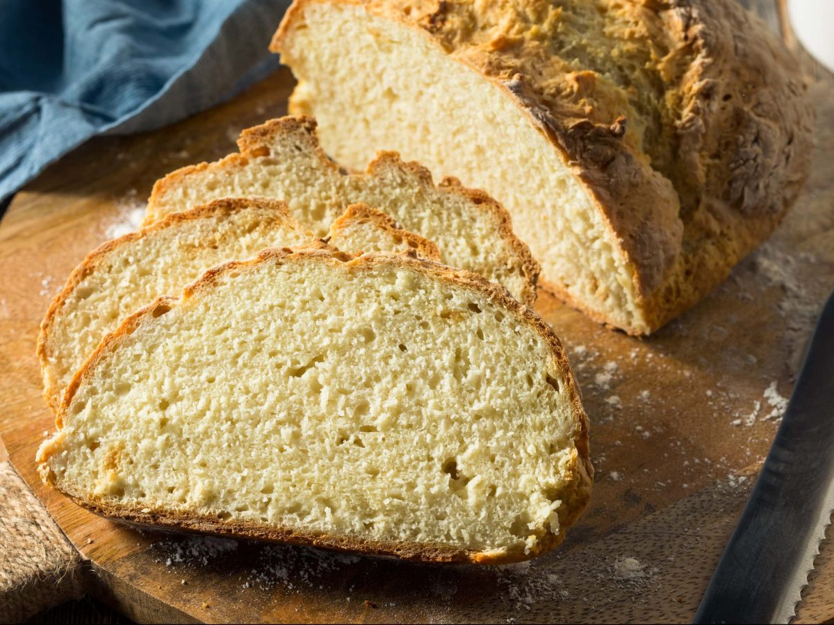 Frontalsicht: ein angeschnittenes Buttermilchbrot auf einem Holzbrettchen.