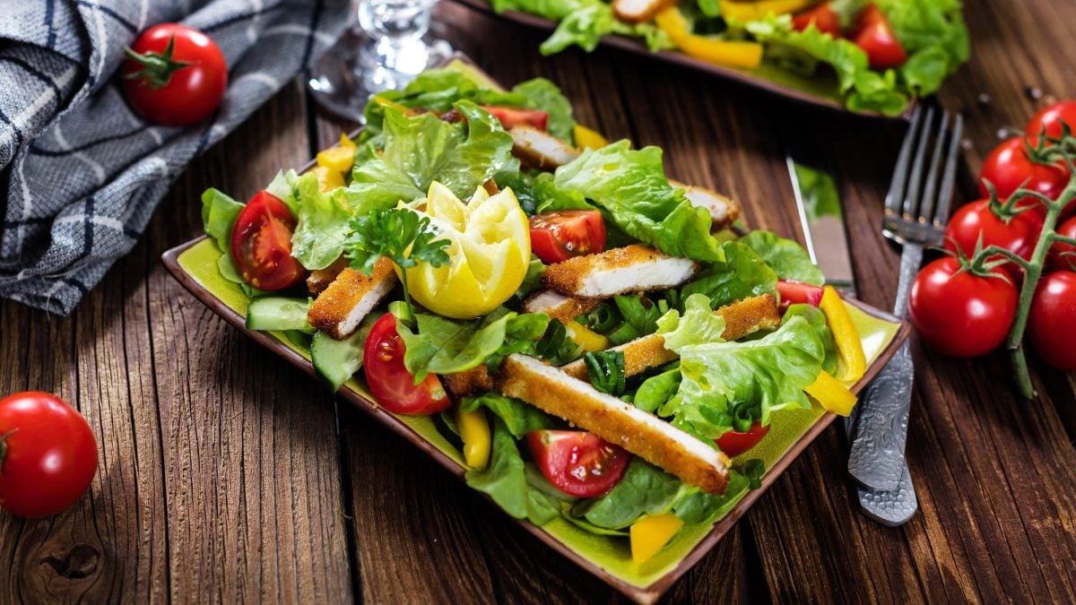 Ein rechteckiger Teller mit buntem Salat, darauf ein in Scheiben geschnittenes Tofu-Schnitzel.