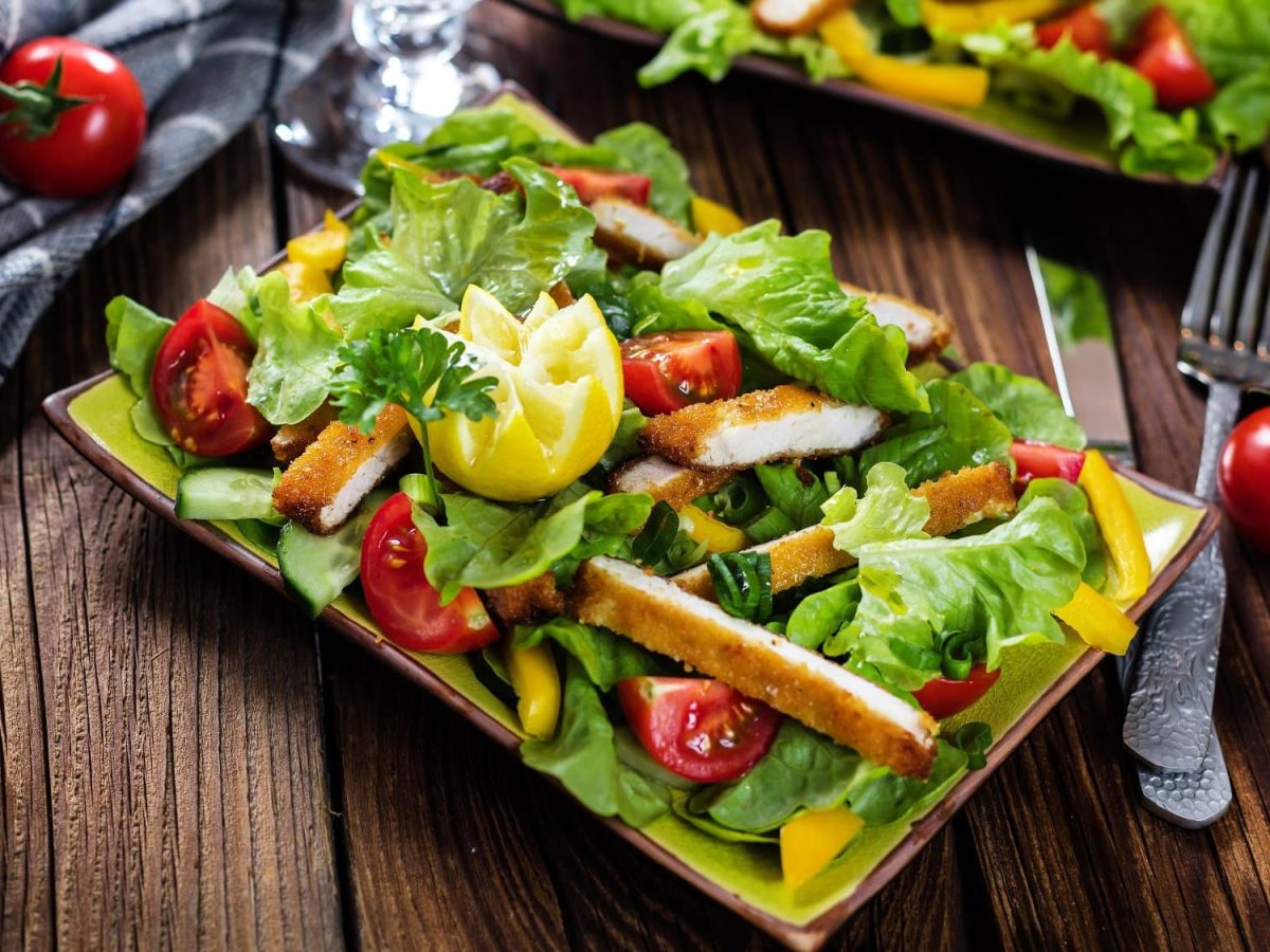 Ein rechteckiger Teller mit buntem Salat, darauf ein in Scheiben geschnittenes Tofu-Schnitzel.