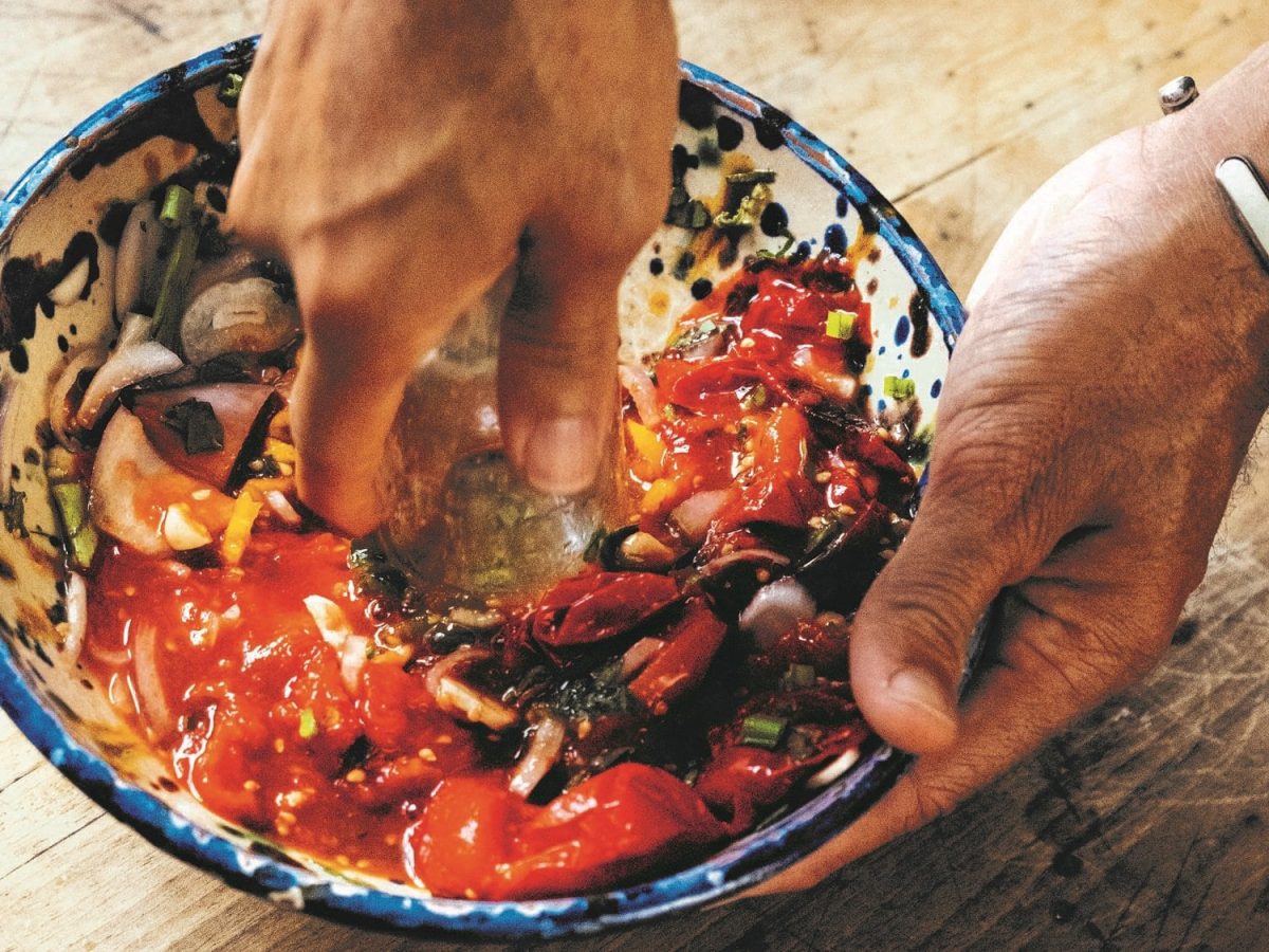 Eine Person zerdrückt Gemüse in einer Schale für ein Tomaten-Choka, man sieht nur ihre Hände.