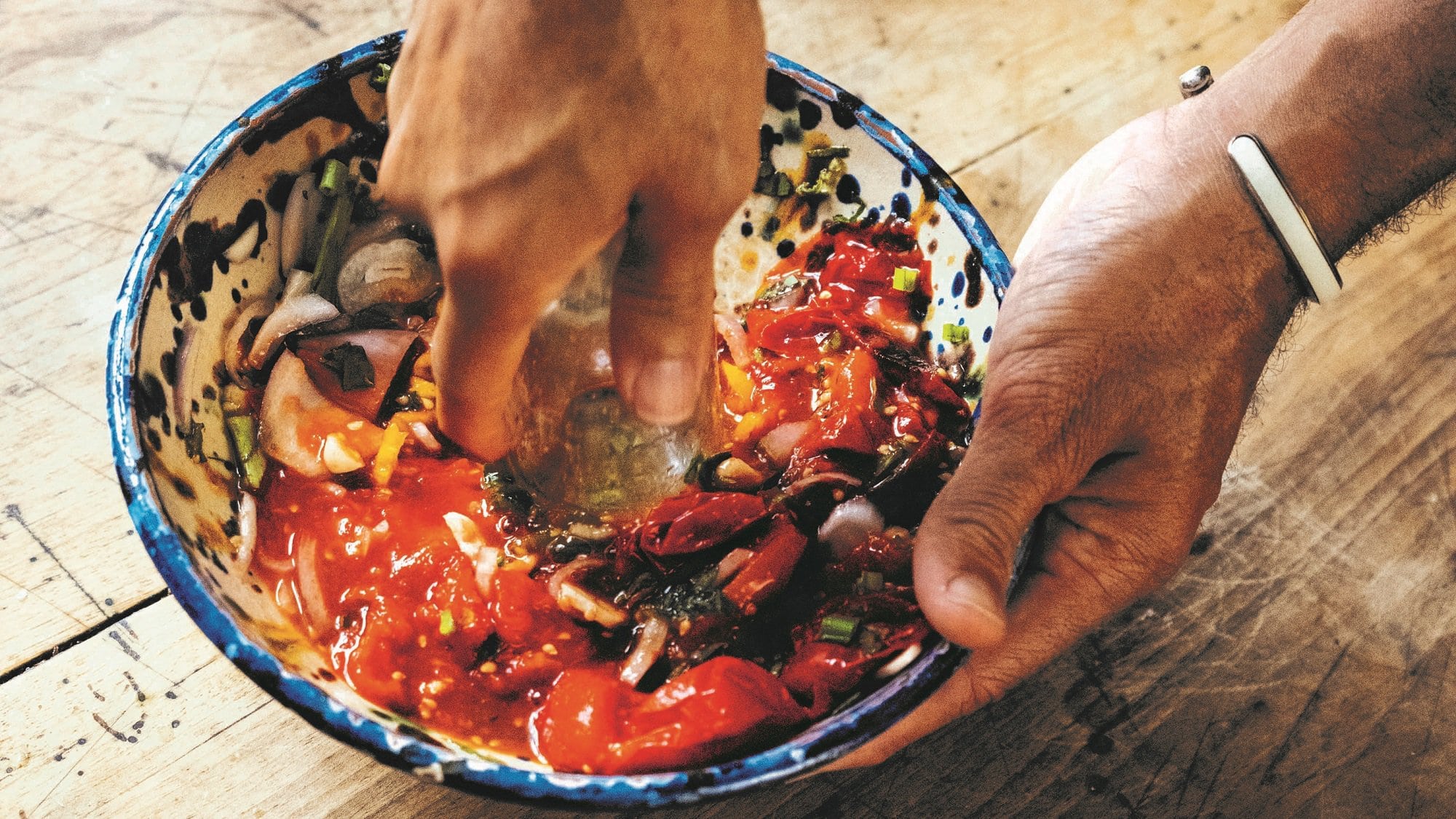 Eine Person zerdrückt Gemüse in einer Schale für ein Tomaten-Choka, man sieht nur ihre Hände.