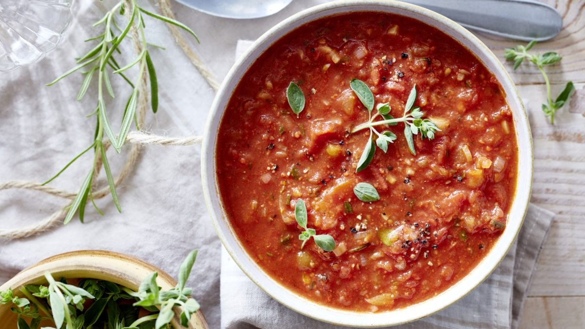 Tomatensuppe mit Rosmarin in einer weißen Schüssel in der Draufsicht vor hellem Untergrund.