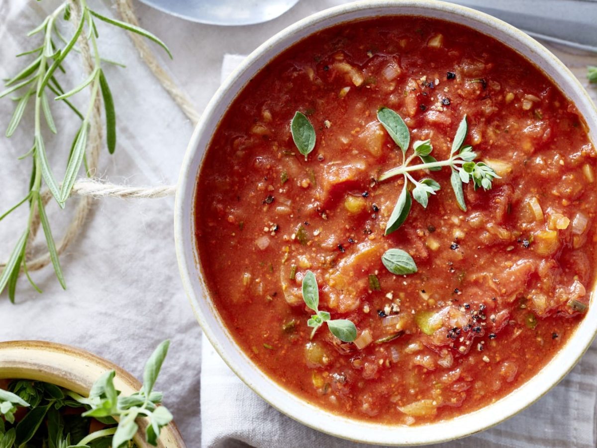 Tomatensuppe mit Rosmarin in einer weißen Schüssel in der Draufsicht vor hellem Untergrund.