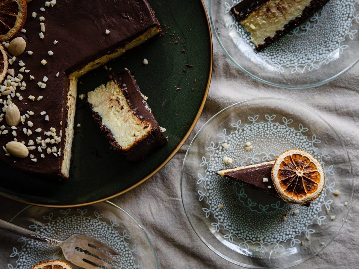 Ein angeschnittener ukrainischer Cheesecake, der auch als Lvivsky Syrnyk bekannt ist, in der Draufsicht, daneben zwei Teller mit je einem Kuchenstück.