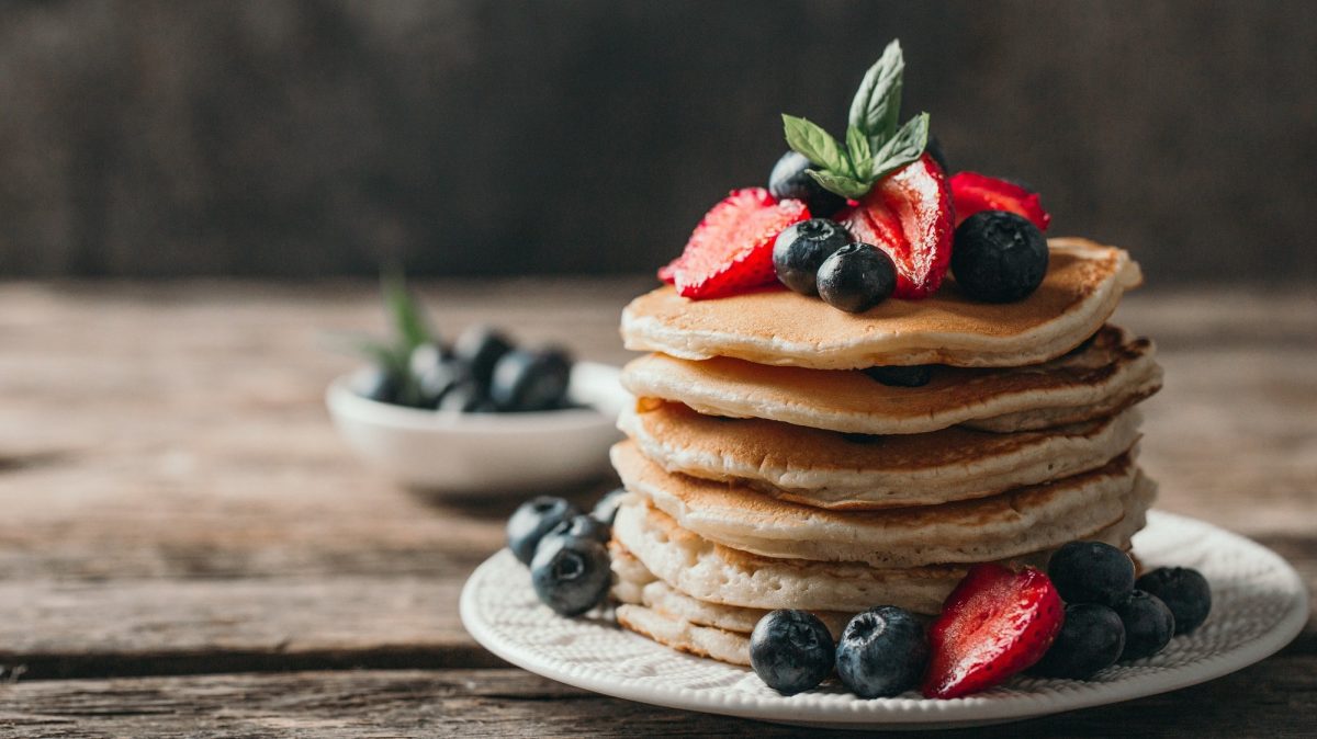 Ein Stapel vegane Apfel-Bananen-Pancakes, verziert mit Blau- und Erdbeeren, auf einem Teller.