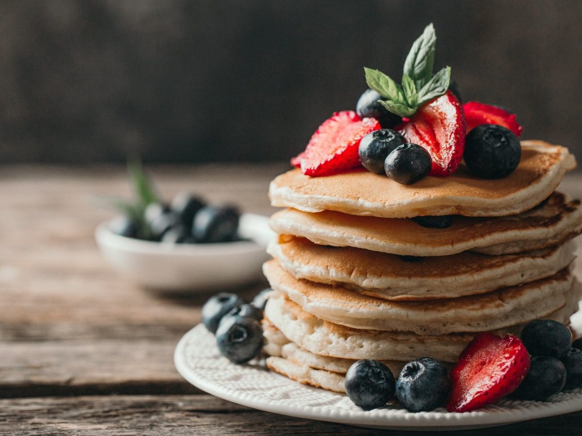 Ein Stapel vegane Apfel-Bananen-Pancakes, verziert mit Blau- und Erdbeeren, auf einem Teller.