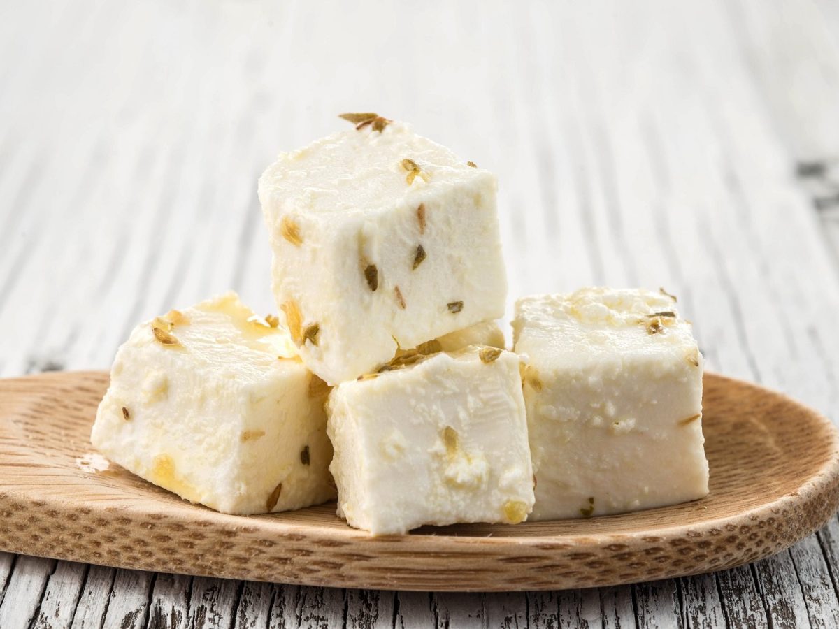 Vegane Feta-Würfel mit Kräutern auf einem Holzlöffel.