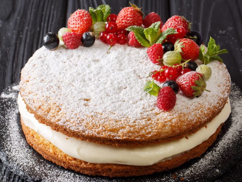 Ein Victoria Sponge Cake mit weißer Sahnecreme, Puderzucker und frischen Beeren.