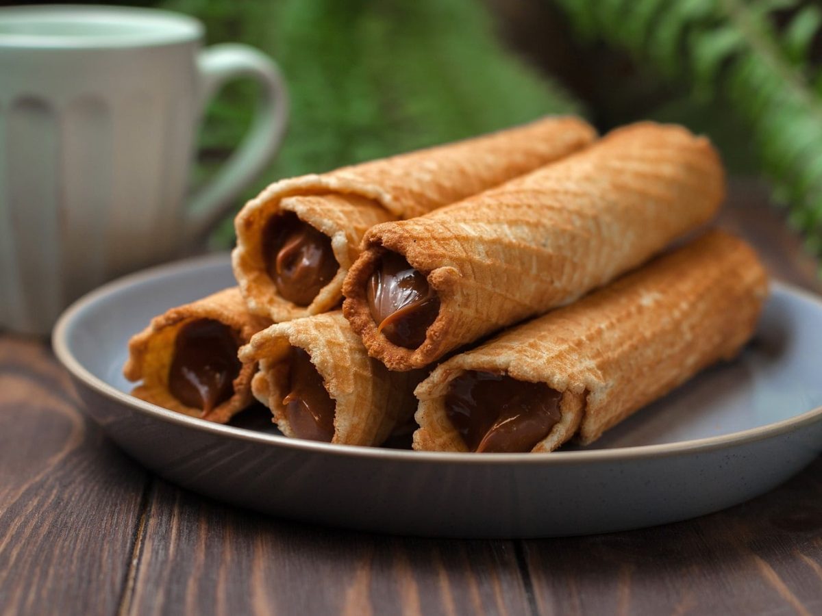 Fünf Waffelrollen mit Dulce de Leche auf einem Holztisch.