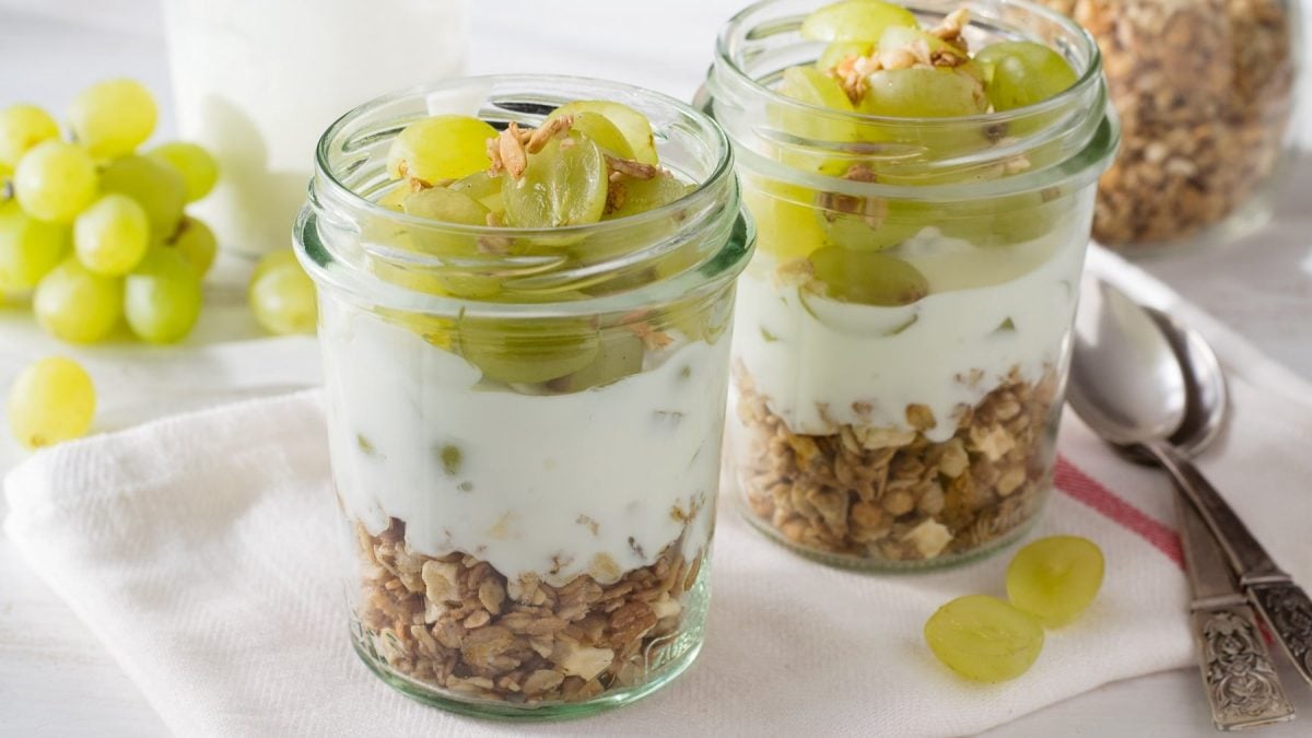 Zwei Gläser mit dem Weintrauben-Granola und Joghurt auf einem hellen Tisch.