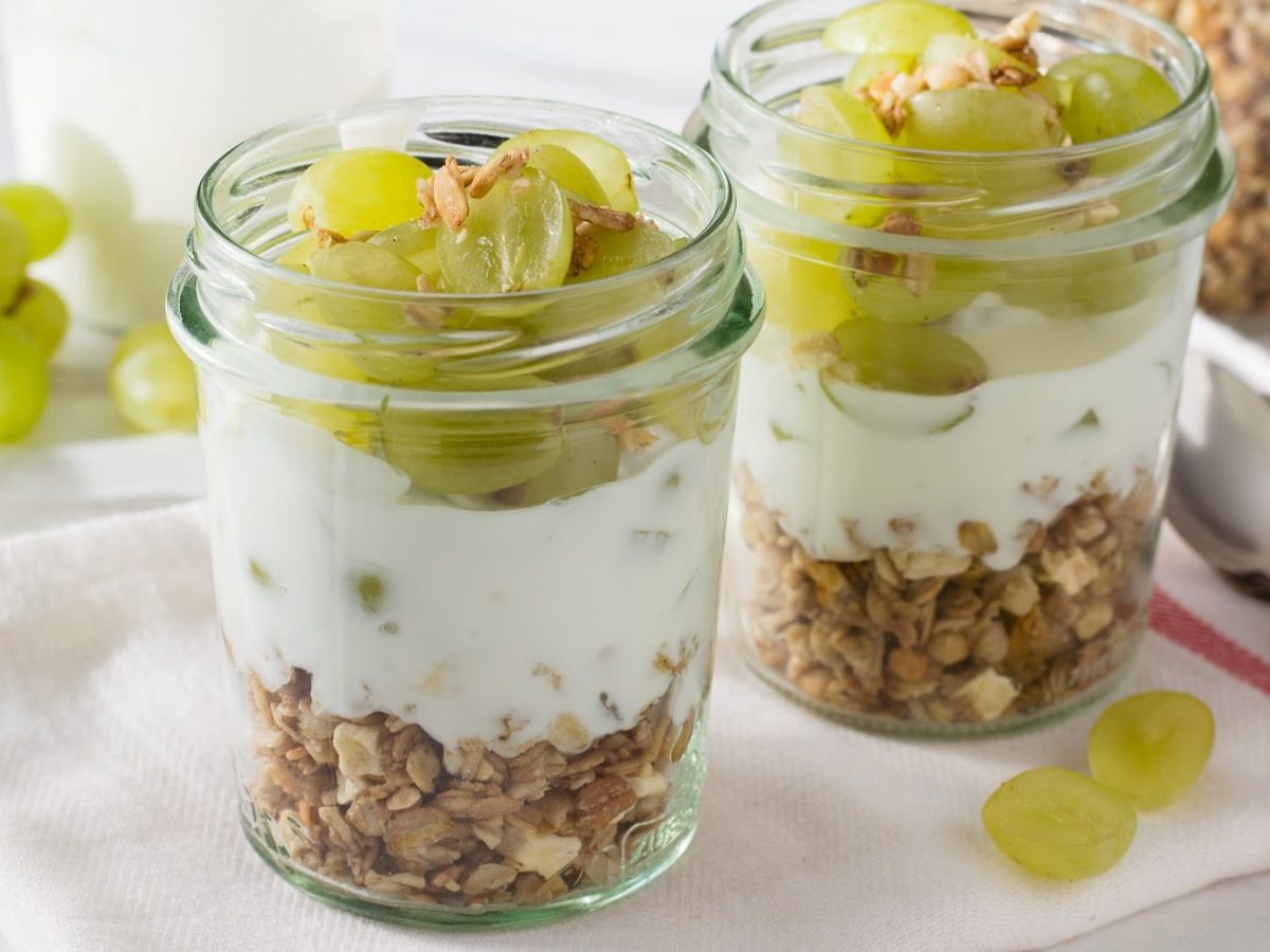 Zwei Gläser mit dem Weintrauben-Granola und Joghurt auf einem hellen Tisch.