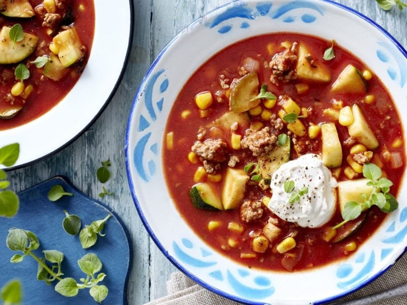 Teller mit Tomaten und Zucchini mit Hackfleisch in der Draufsicht. es handelt sich um einen Eintopf.