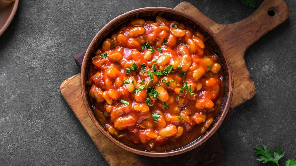 Ein Teller afrikanischer Bohneneintopf mit einer Erdnuss-Tomatensauce und Kräutern bestreut auf einem Brett, Draufsicht.