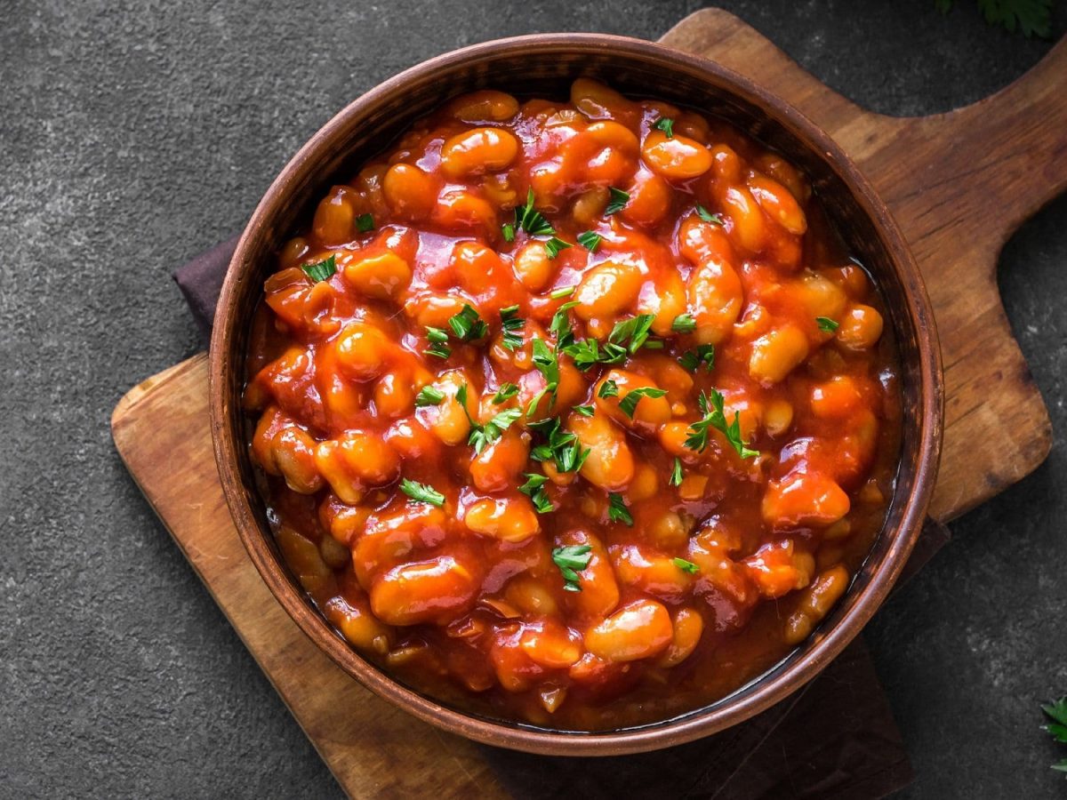 Ein Teller afrikanischer Bohneneintopf mit einer Erdnuss-Tomatensauce und Kräutern bestreut auf einem Brett, Draufsicht.