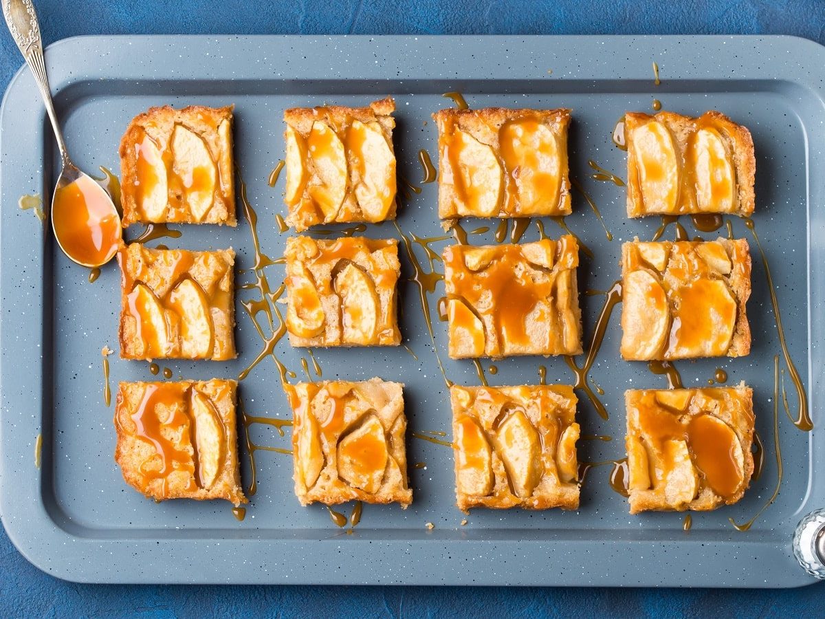 Ein blaues Backblech mit Apfel-Zimt-Blondies auf einem blauen Tisch.