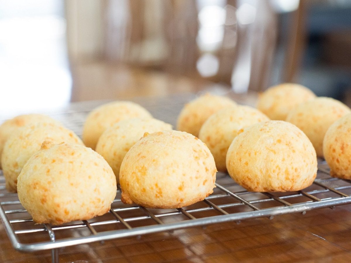 Frontalsicht: auf einem Untergrund aus Holz steht ein Gitter auf dem runde Parmesan-Brötchen abkühlen.