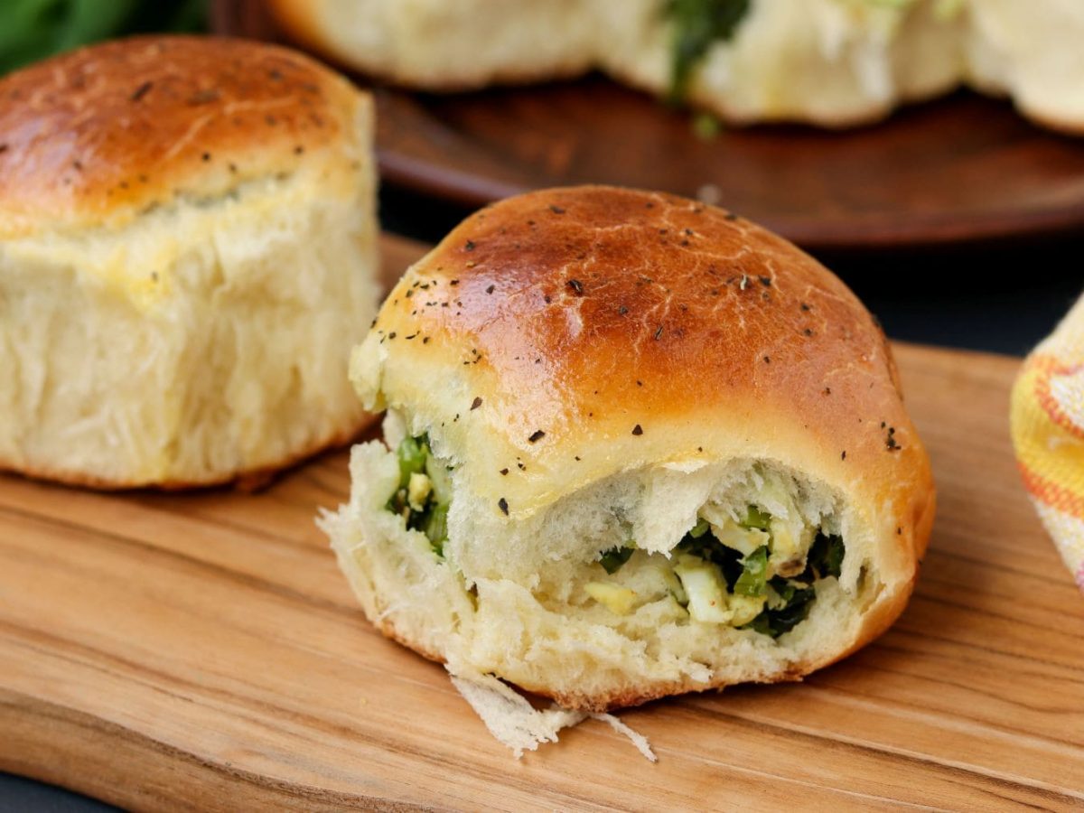 Gefüllte Bärlauch-Brioche mit Ei auf Holzbrett auf Holztisch. Frontalansicht.