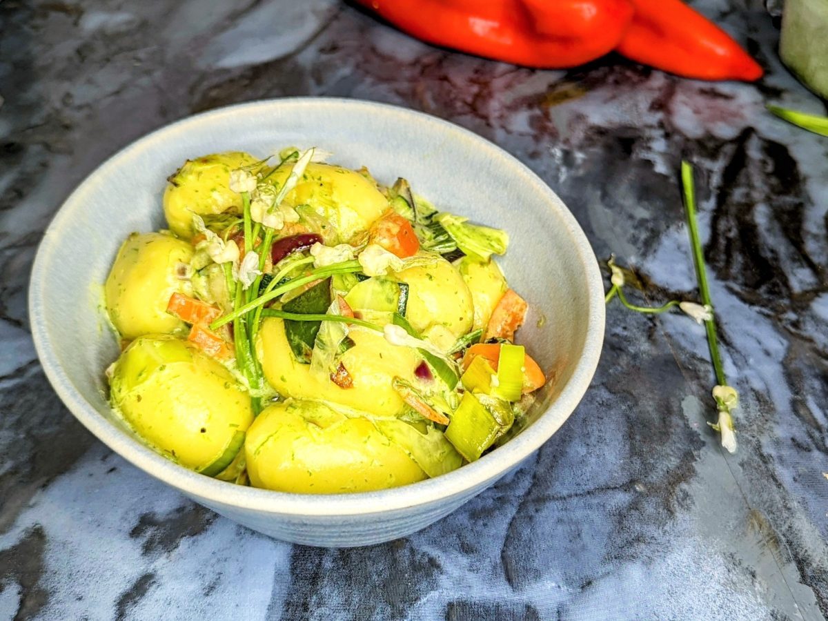 Eine schale mit den Gnocchi auf einem Marmortisch. Im Hintergrund Paprika und Pesto.