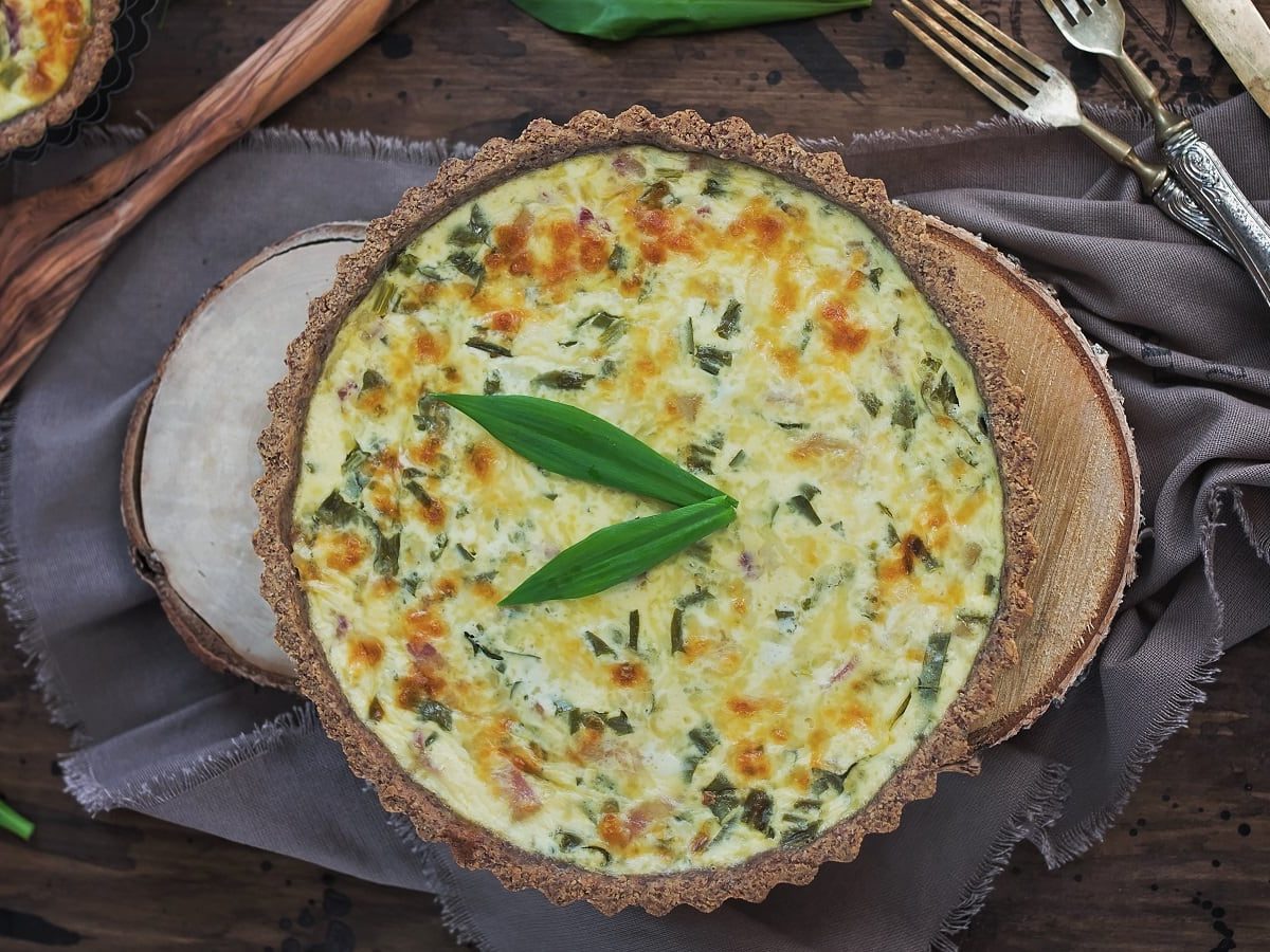 Eine Tarteform mit Bärlauch-Quiche neben Besteck.