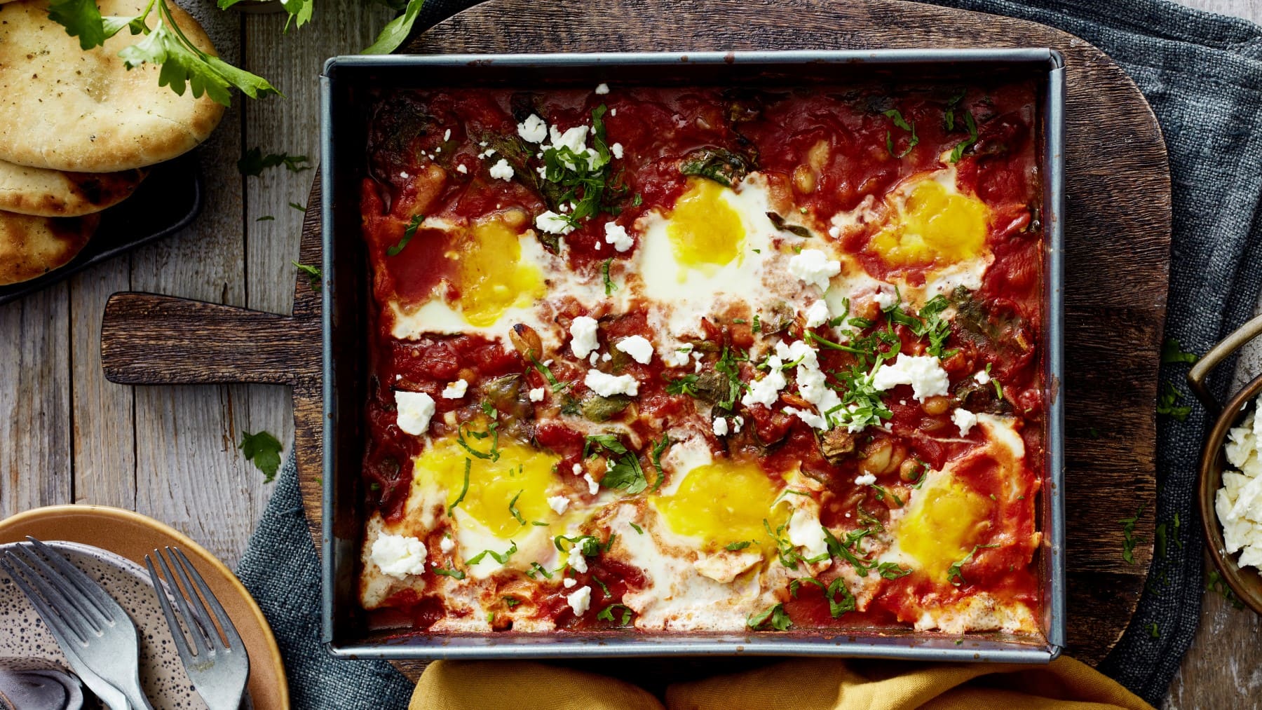 Eine Backform mit Ofen-Shakshuka mit Spinat auf einem gedeckten Tisch.