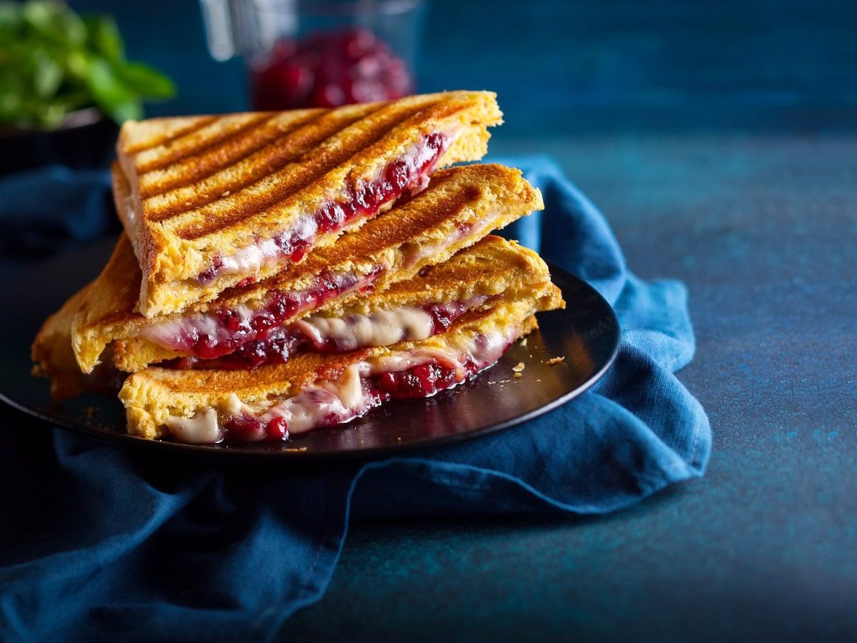 Frontal: zwei schräg angeschnittene Cheddar-Toasts mit Zwiebel-Chutney auf blauem Untergrund.