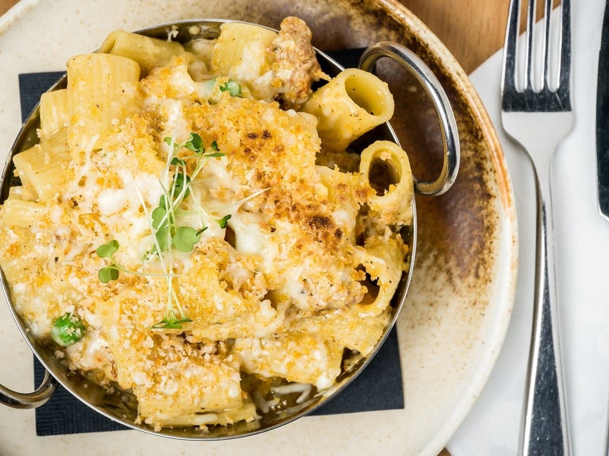 Ein runder beiger Teller mit Chorizo Carbonara neben Messer und Gabel.