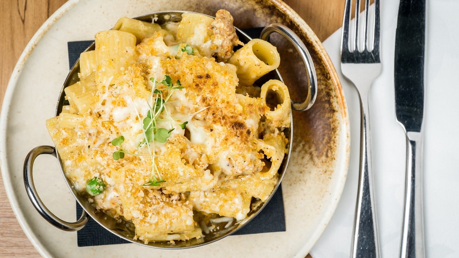 Ein runder beiger Teller mit Chorizo Carbonara neben Messer und Gabel.