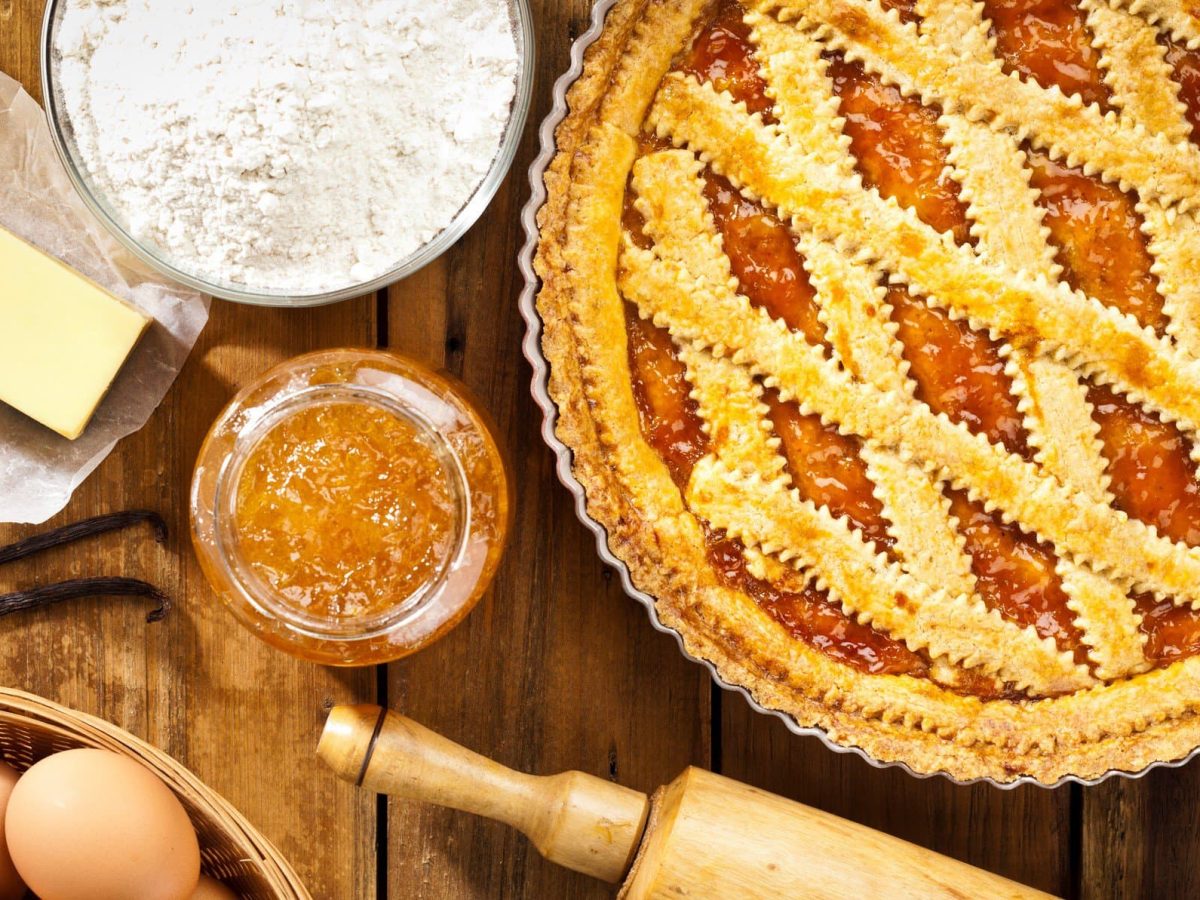 Crostata arancia auf Holztisch mit Zutaten arrangiert. Draufsicht.