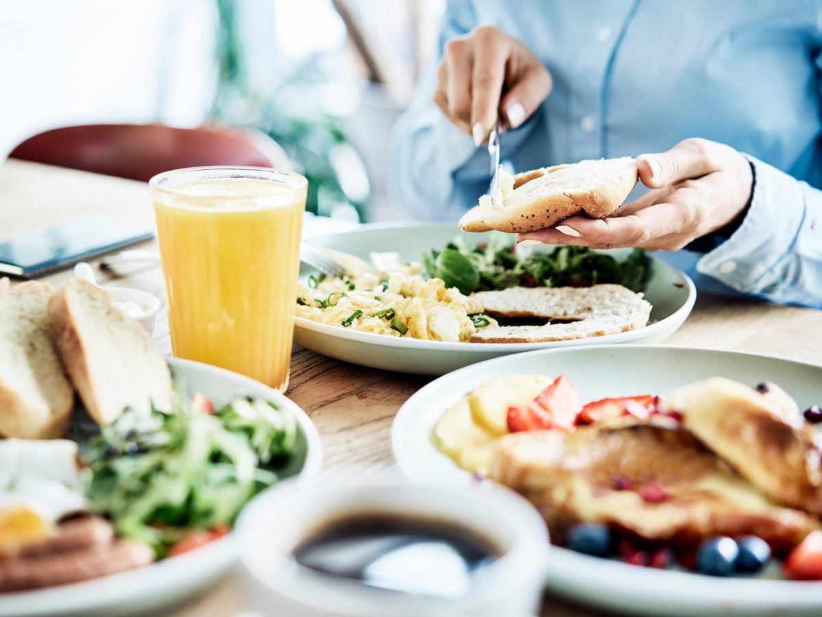 Die beliebtesten Brunch-Lokale Deutschlands: Eine Frau sitzt einem gedeckten Frühstückstisch, schmiert sich ein Brötchen, vor ihr volle Teller.