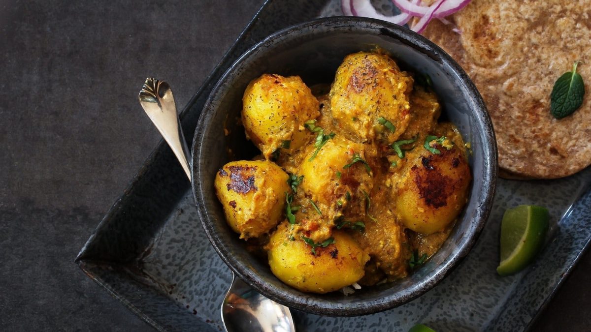 Eine schwarze Schüssel mit Dum Aloo auf einem dunklen Tisch.