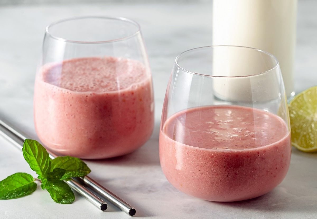 Zwei Gläser mit Himbeer-Tahini-Shake neben frischen Limetten.