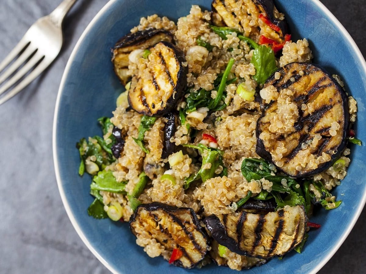 Eine blaue Schüssel mit Quinoa-Salat mit gegrillter Aubergine auf einem grauen Tisch.