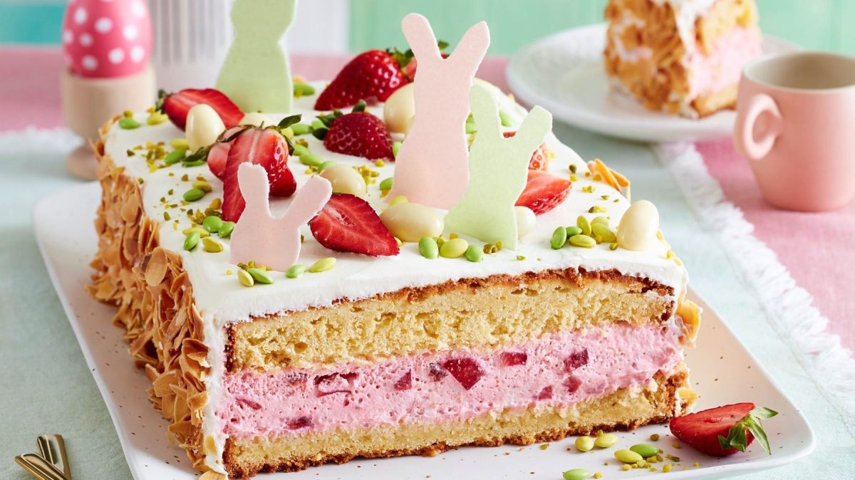 Auf einem Teller ist eine Erdbeer-Ostertorte angerichtet. Sie ist mit Erdbeeren, Pistazien und Osterhasen aus Esspapier verziert.