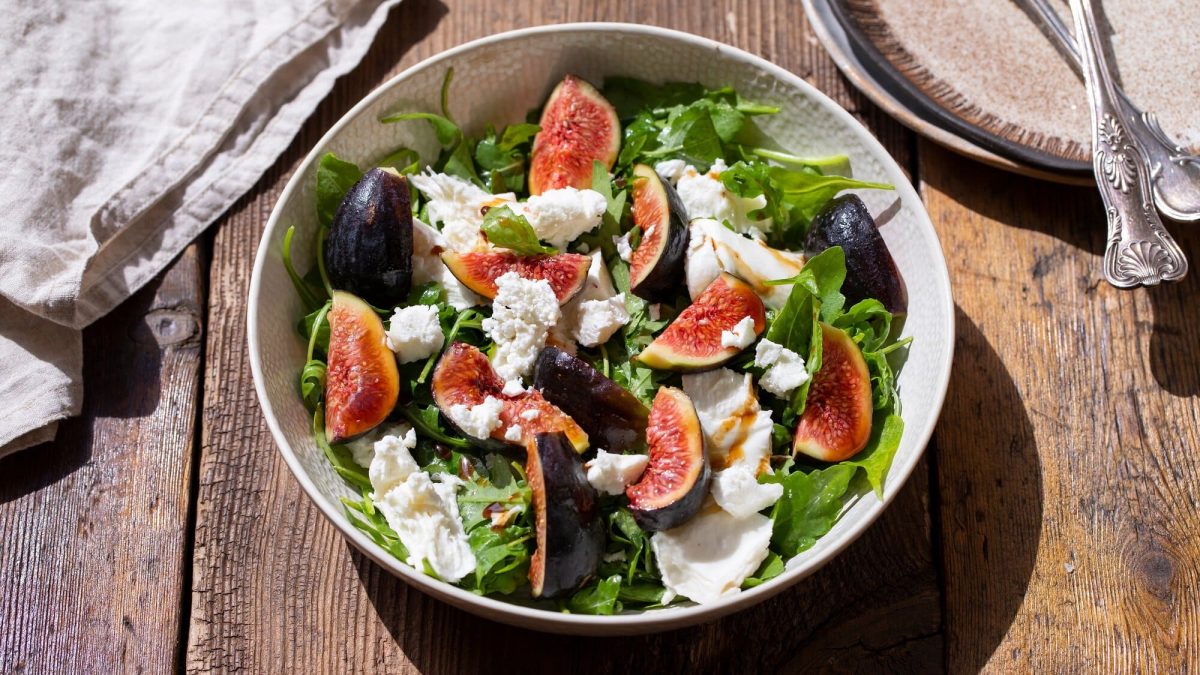 Draufsicht: Eine Schüssel Feigen-Mozzarella-Salat steht auf einem Holztisch.