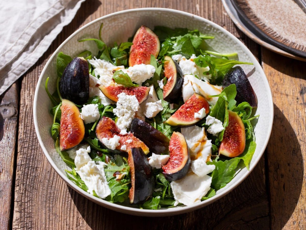 Draufsicht: Eine Schüssel Feigen-Mozzarella-Salat steht auf einem Holztisch.