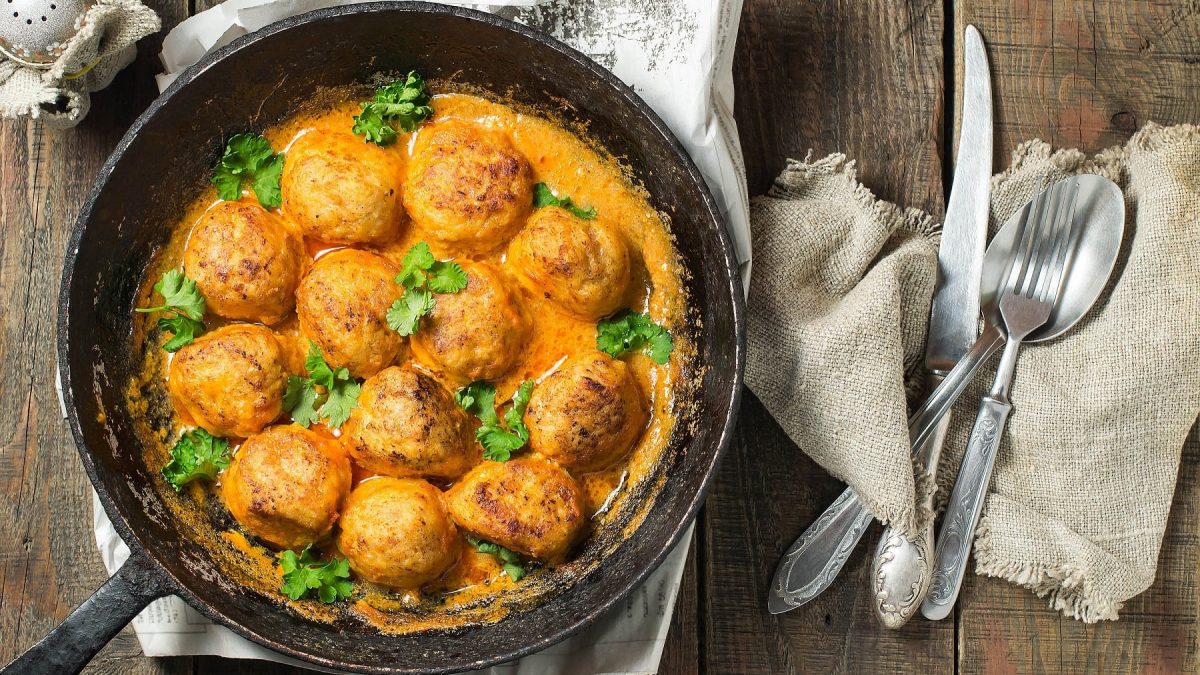 Eine schwarze Pfanne mit den Garnelen-Huhn-Bällchen in Currysauce mit Koriander bestreut.