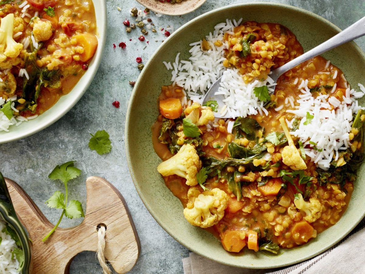 In einer Schüssel ist ein Grünkohl-Linsen-Curry angerichtet. Es wird mit Grünkohl, Tomaten und Ingwer verfeinert.