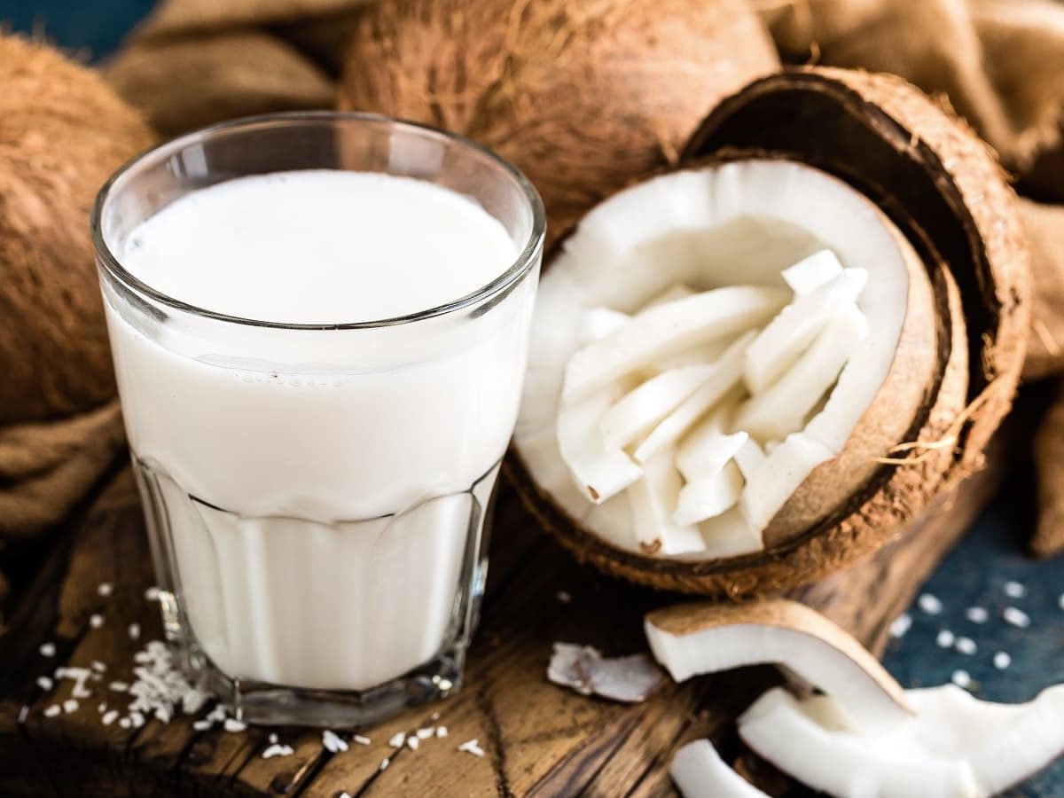 Ein Glas mit heißer Kokosschokolade neben einer frischen Kokosnuss.